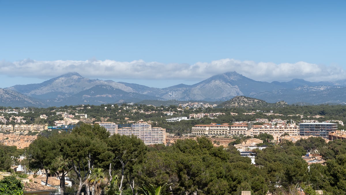 Vue aérienne d'un paysage méditerranéen avec pinèdes, résidences et montagnes lointaines sous un ciel clair.