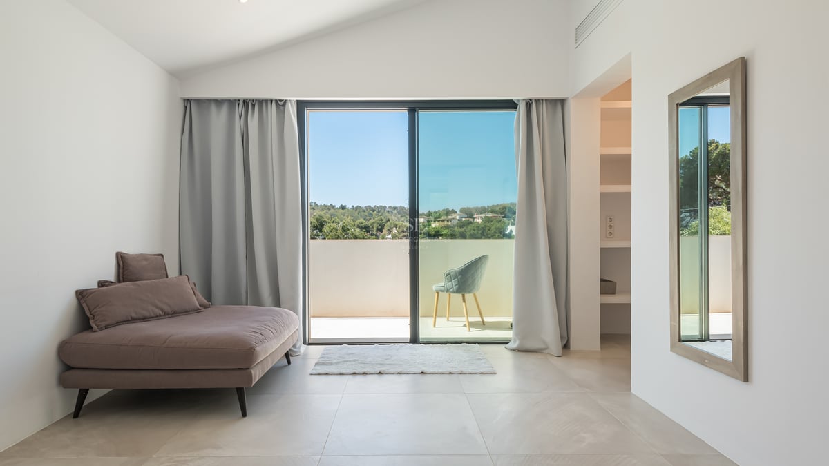 Chambre moderne avec baies vitrées ouvrant sur une terrasse ensoleillée avec vue sur la nature.