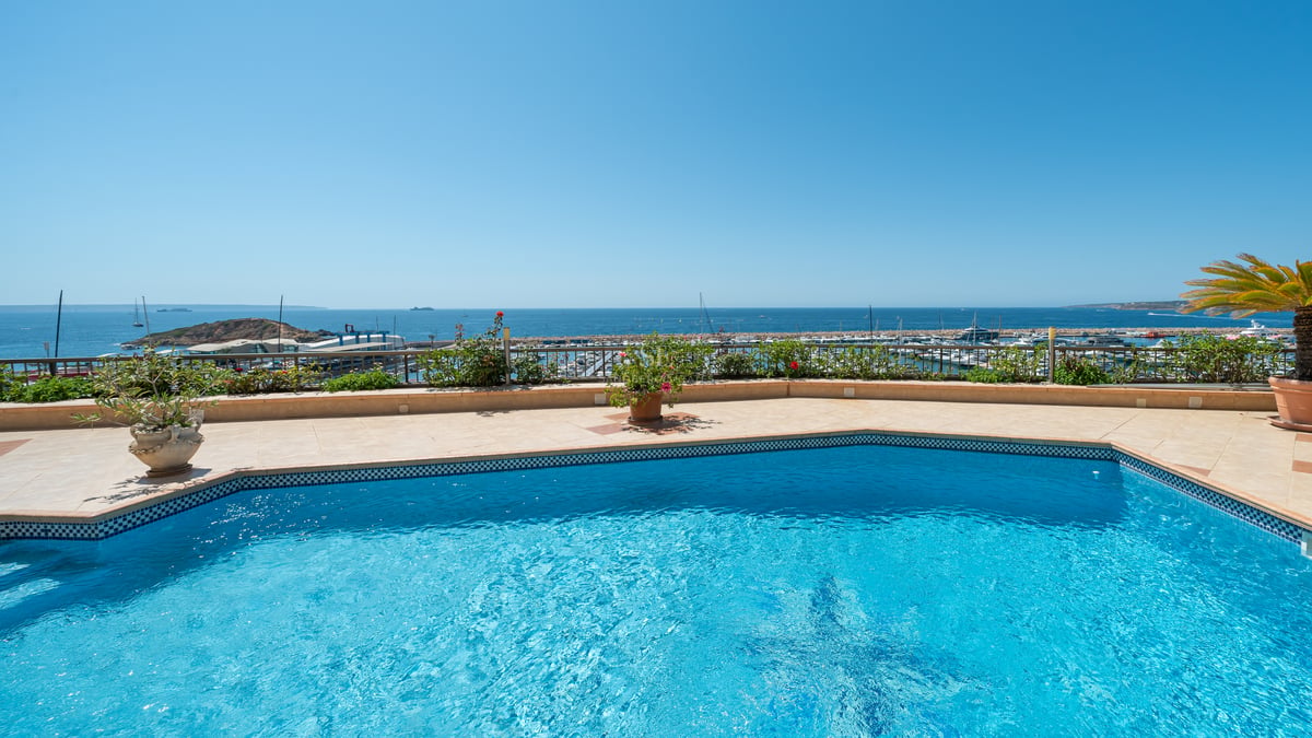 Terrasse avec piscine en mosaïque bleue et vue sur un port de plaisance méditerranéen sous un ciel bleu.