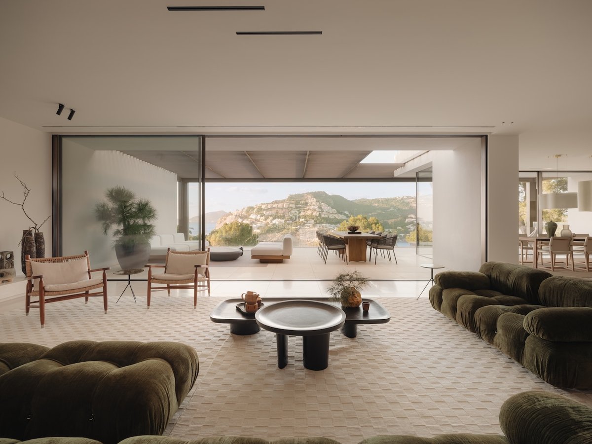 Salon de luxe avec canapés en velours vert et baies vitrées ouvrant sur une terrasse de montagne panoramique.