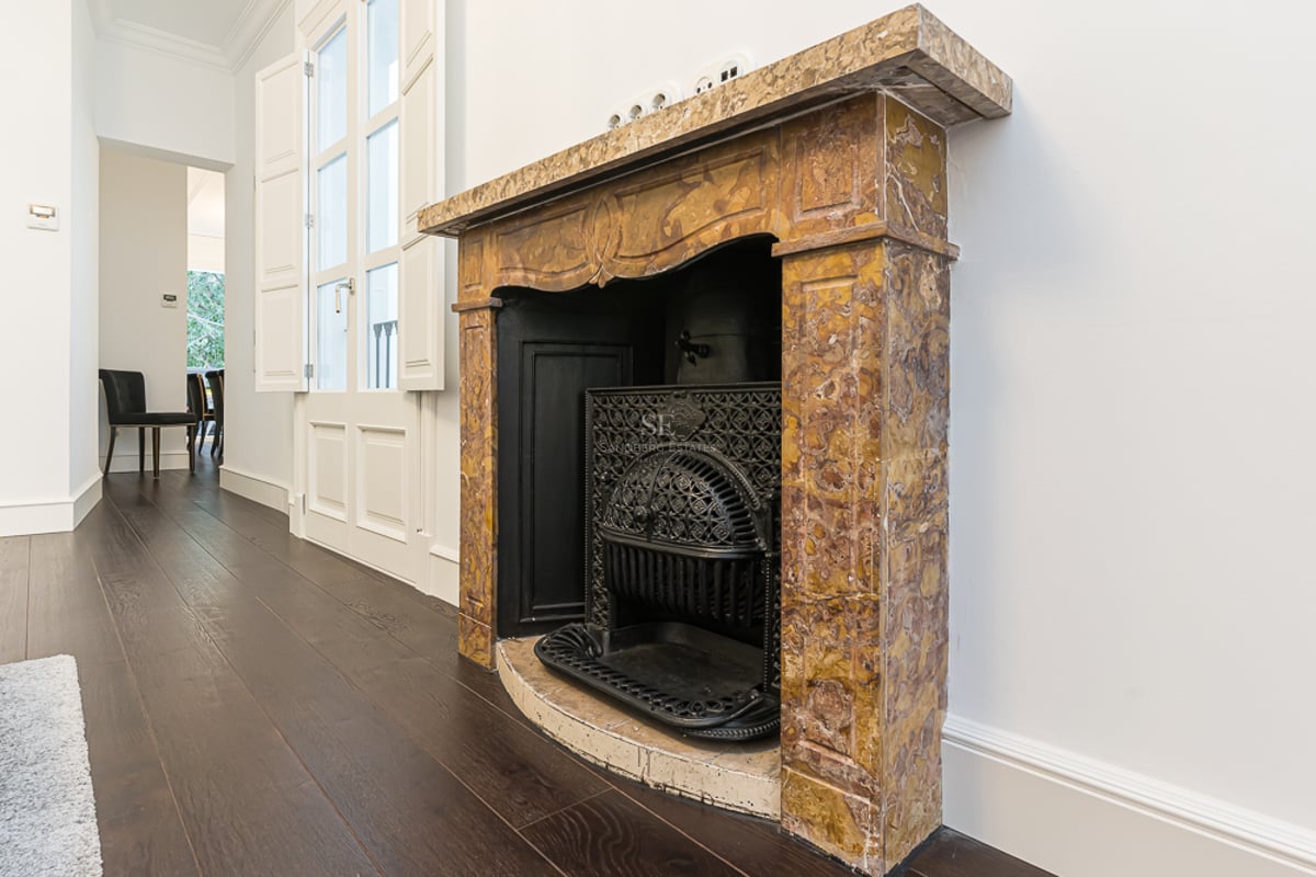 Cheminée en marbre jaune ornée avec grille en fonte noire sur parquet sombre et murs blancs.