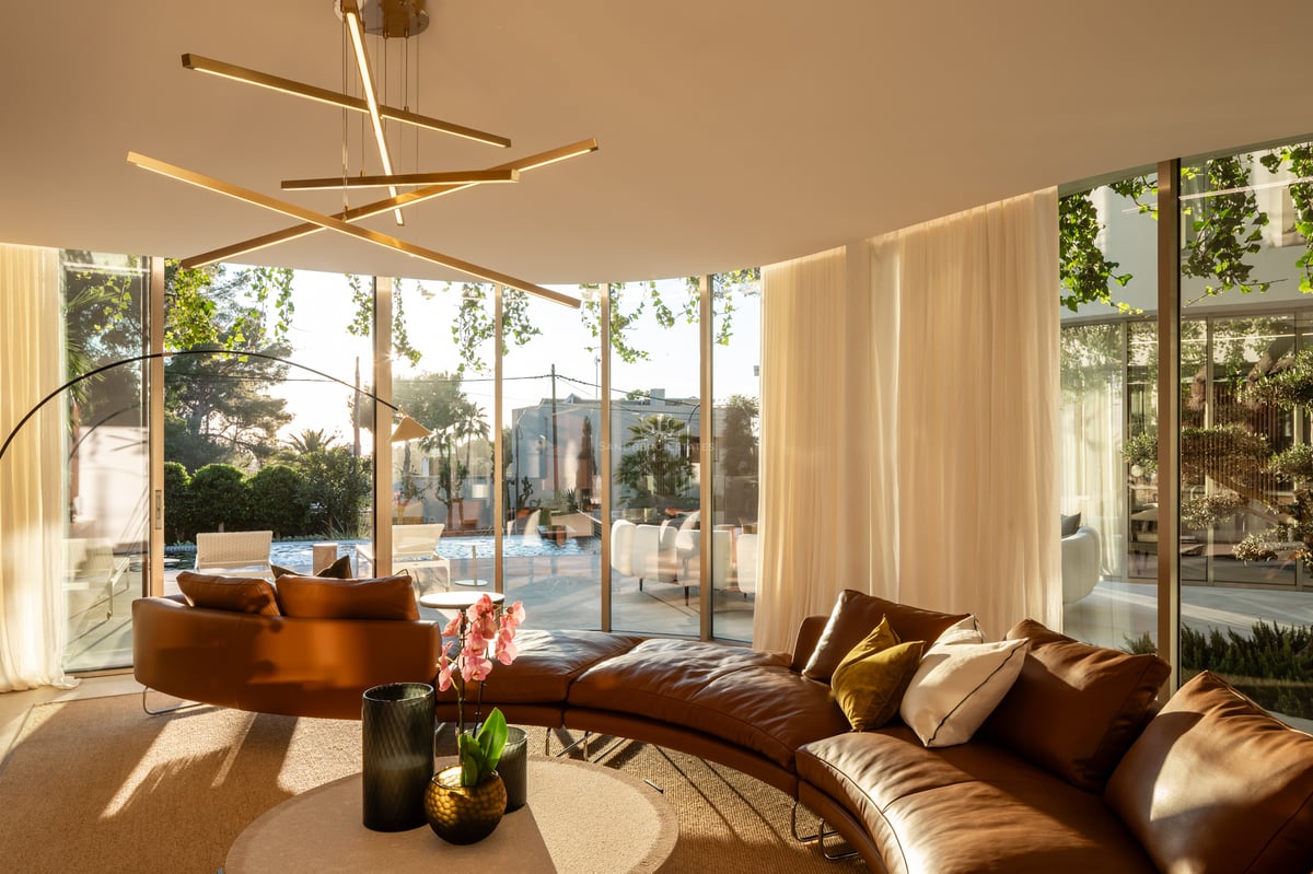 Salon luxueux avec canapé incurvé en cuir, luminaire design et grandes baies vitrées donnant sur la piscine.