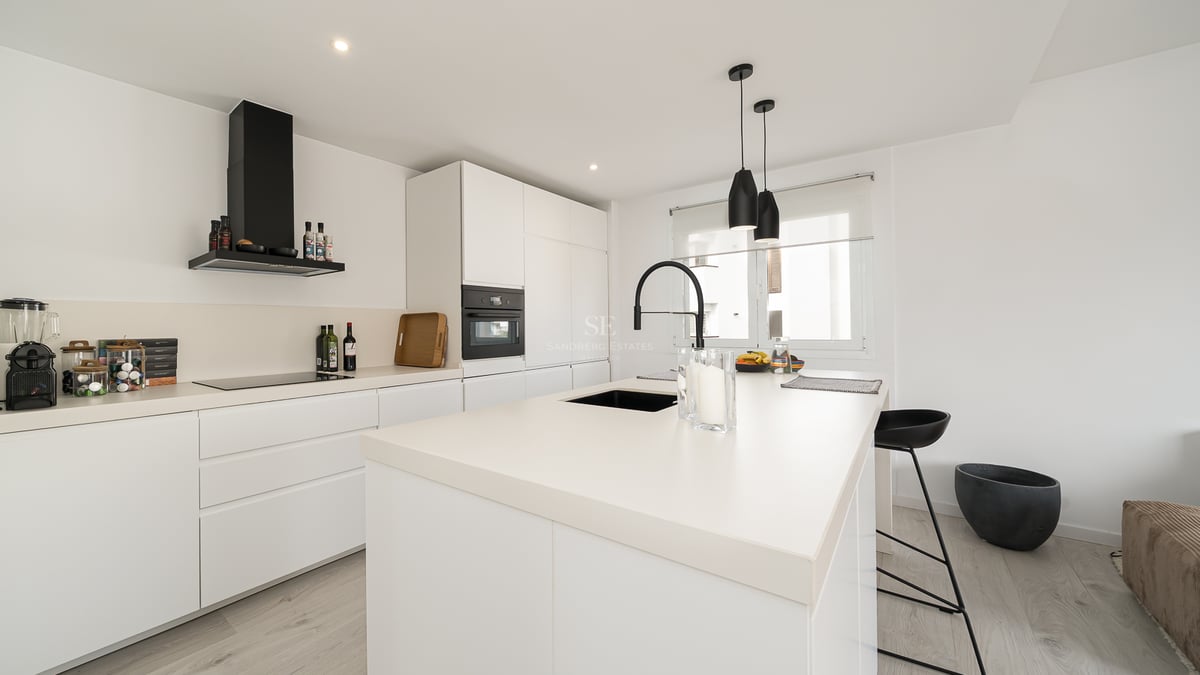 Cuisine blanche moderne avec un grand îlot, un robinet noir et des appareils électroménagers intégrés.
