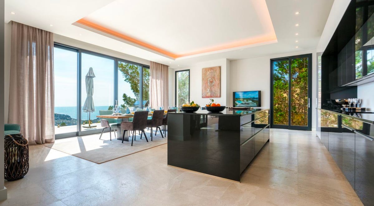Cuisine et salle à manger modernes avec îlot noir brillant et grandes fenêtres offrant une vue sur la mer.