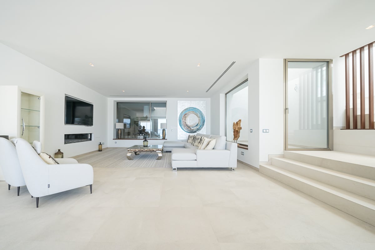 Salon minimaliste lumineux avec canapé blanc, sol en pierre, cheminée linéaire et art moderne.