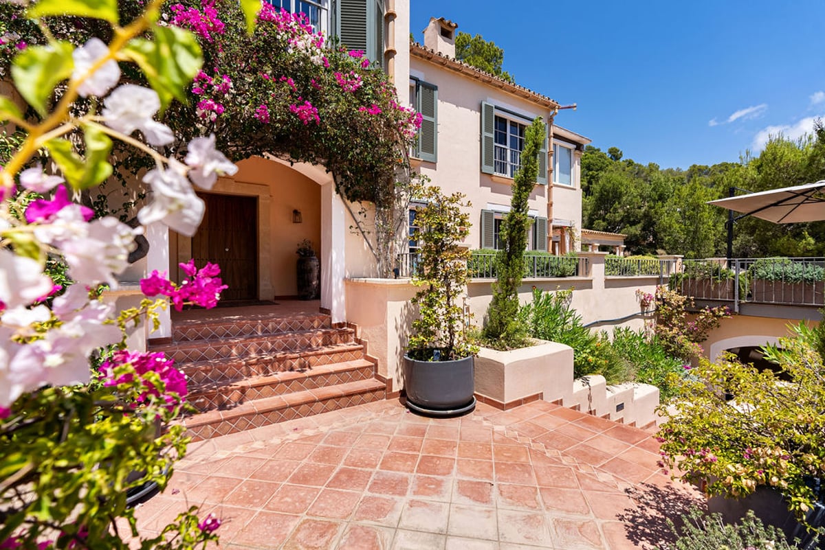 Marches en terre cuite menant à une porte en bois d'une villa encadrée de bougainvilliers roses.
