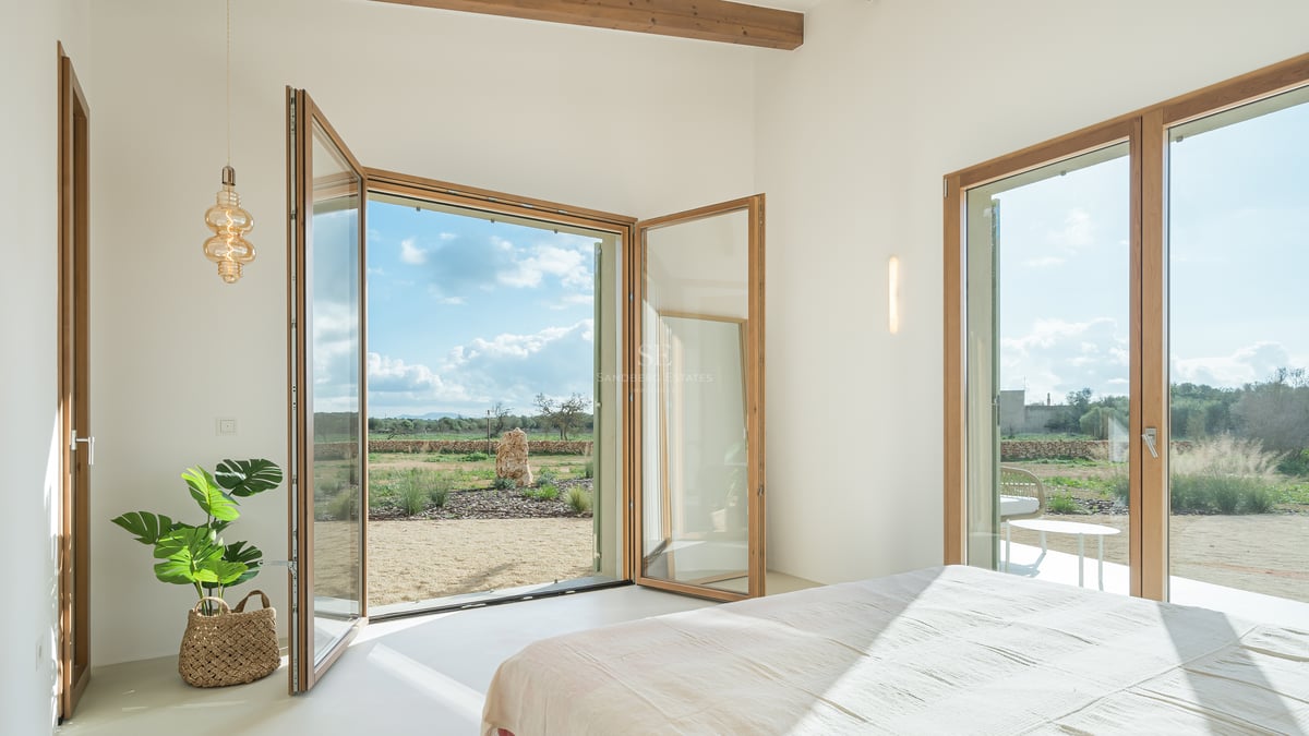 Bright bedroom featuring large wood-framed glass doors opening onto a Mediterranean landscape with olive trees.