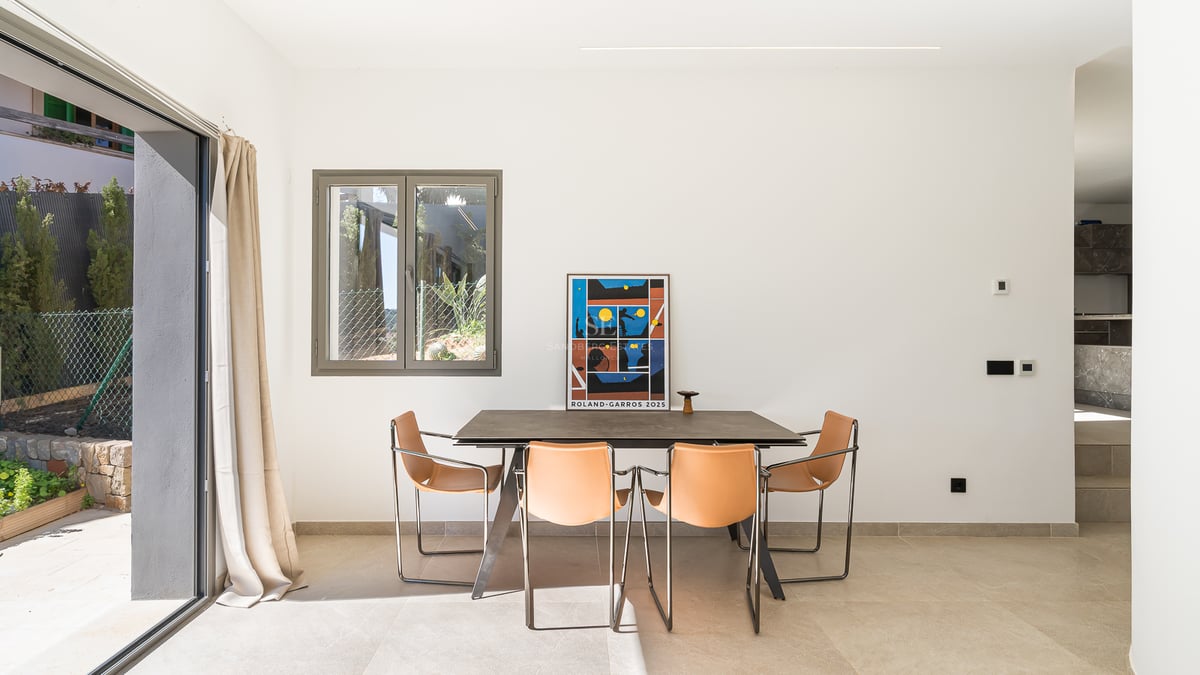 Salle à manger moderne avec table en pierre, chaises en cuir fauve et grandes baies vitrées coulissantes.