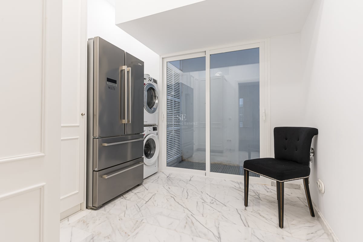 Buanderie avec réfrigérateur en inox, lave-linge et sèche-linge superposés, et sol en marbre blanc.