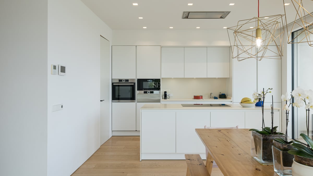 Cuisine minimaliste blanche avec îlot, appareils intégrés, parquet en chêne clair et table à manger en bois.
