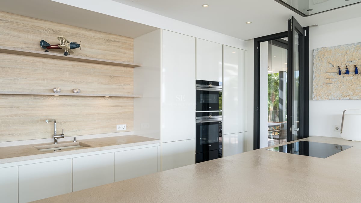 Cuisine moderne aux meubles blancs, dosseret en bois, îlot en pierre et appareils encastrés.