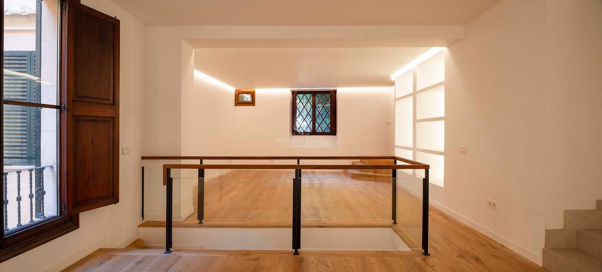 Palier intérieur moderne avec parquet en chêne clair, garde-corps en verre et éclairage indirect chaleureux.