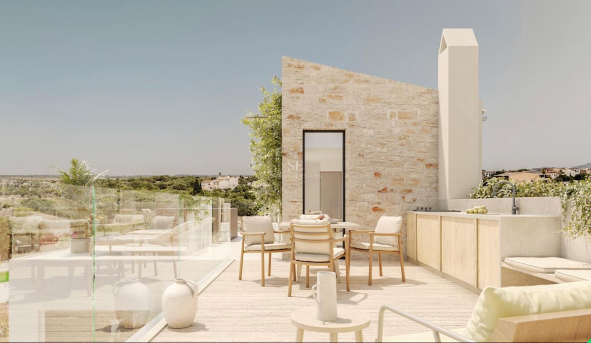 Terrasse moderne en pierre avec coin repas, cuisine extérieure et garde-corps en verre donnant sur la campagne.