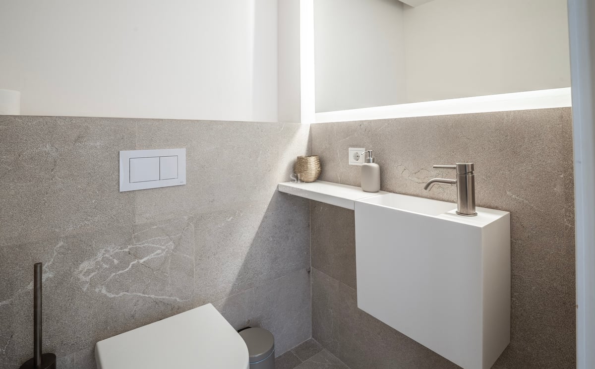Cabinet de toilette moderne avec carreaux de pierre texturés, lavabo suspendu blanc et grand miroir rétroéclairé.