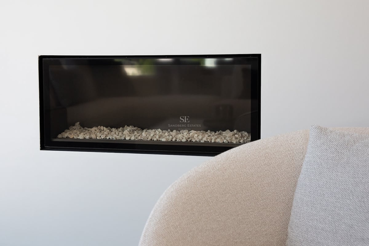 Gros plan d'une cheminée rectangulaire à cadre noir intégrée dans un mur blanc avec des pierres blanches à l'intérieur.
