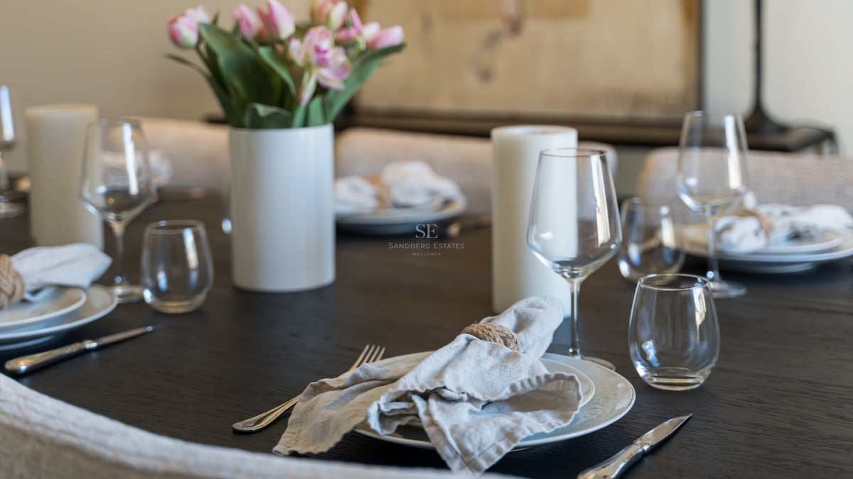 Close-up of a dark wooden dining table set with white plates, linen napkins, crystal glasses, and pink tulips.