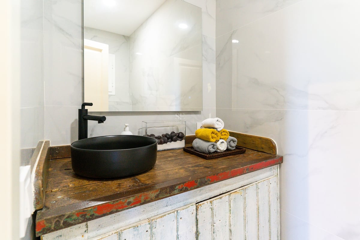 Vasque noir mat sur meuble en bois rustique avec carrelage effet marbre et grand miroir.