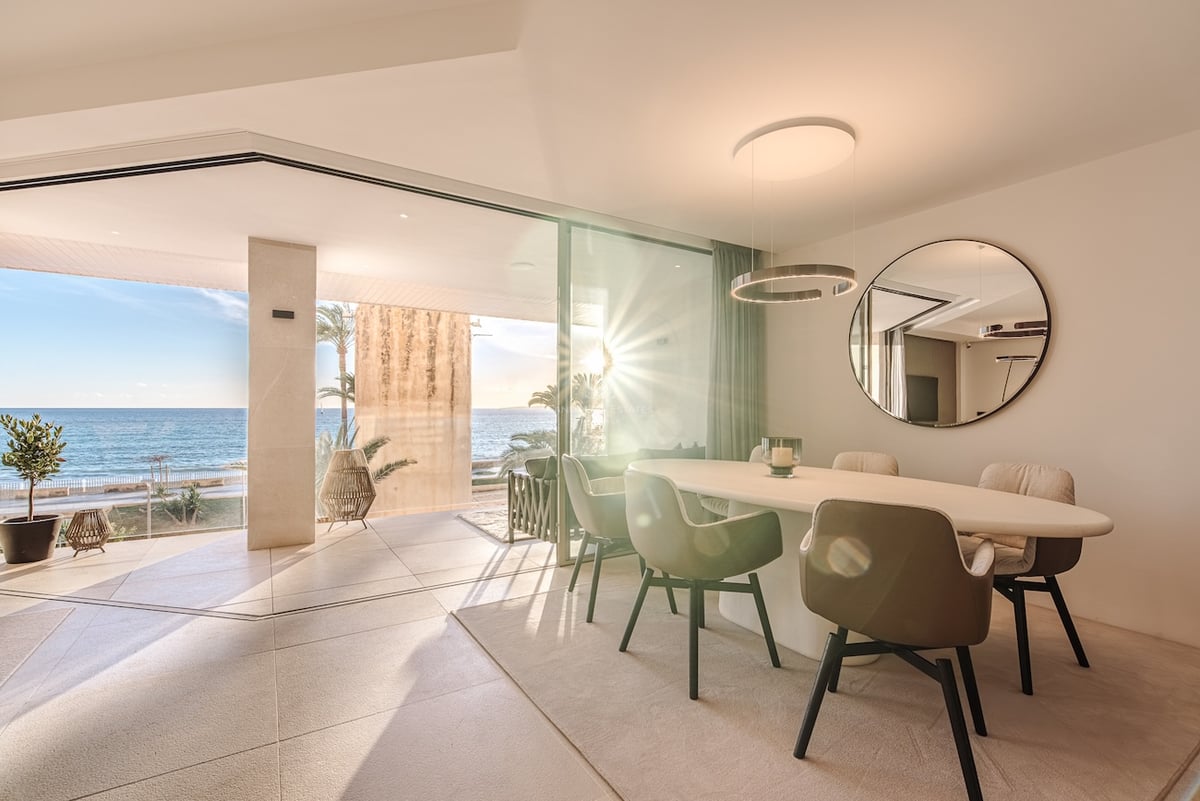 Moderner Essbereich mit ovalem Tisch und Glasschiebetüren, die auf eine sonnige Terrasse am Meer führen.