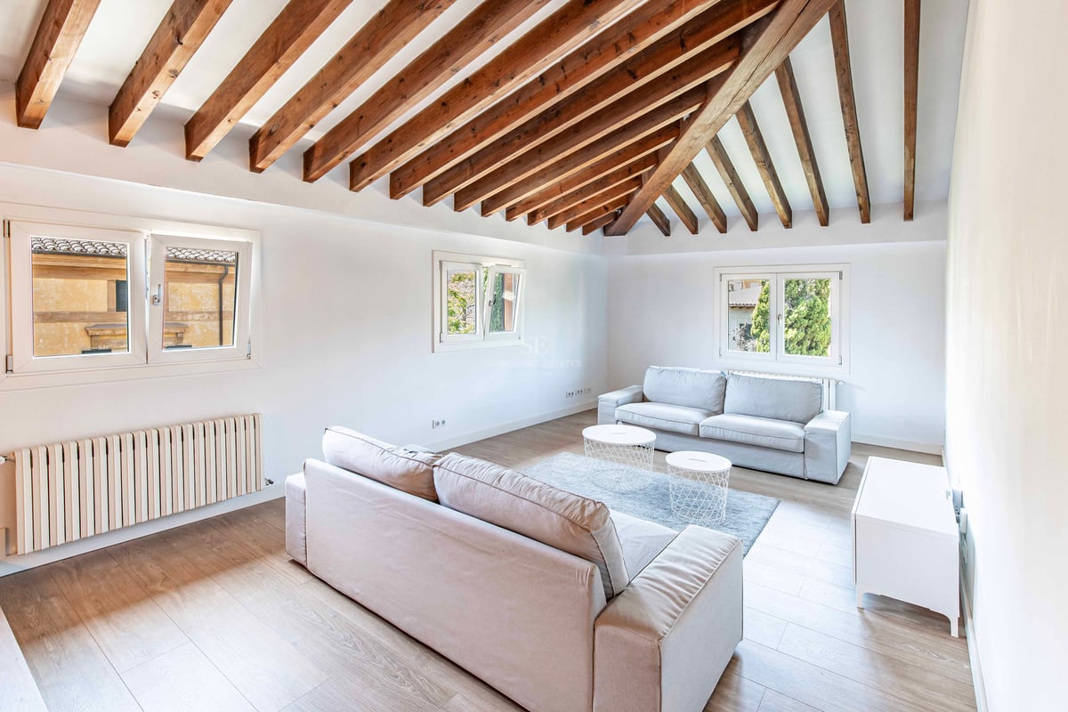 Salon lumineux avec plafond voûté en poutres de bois sombre, canapés neutres et parquet clair.