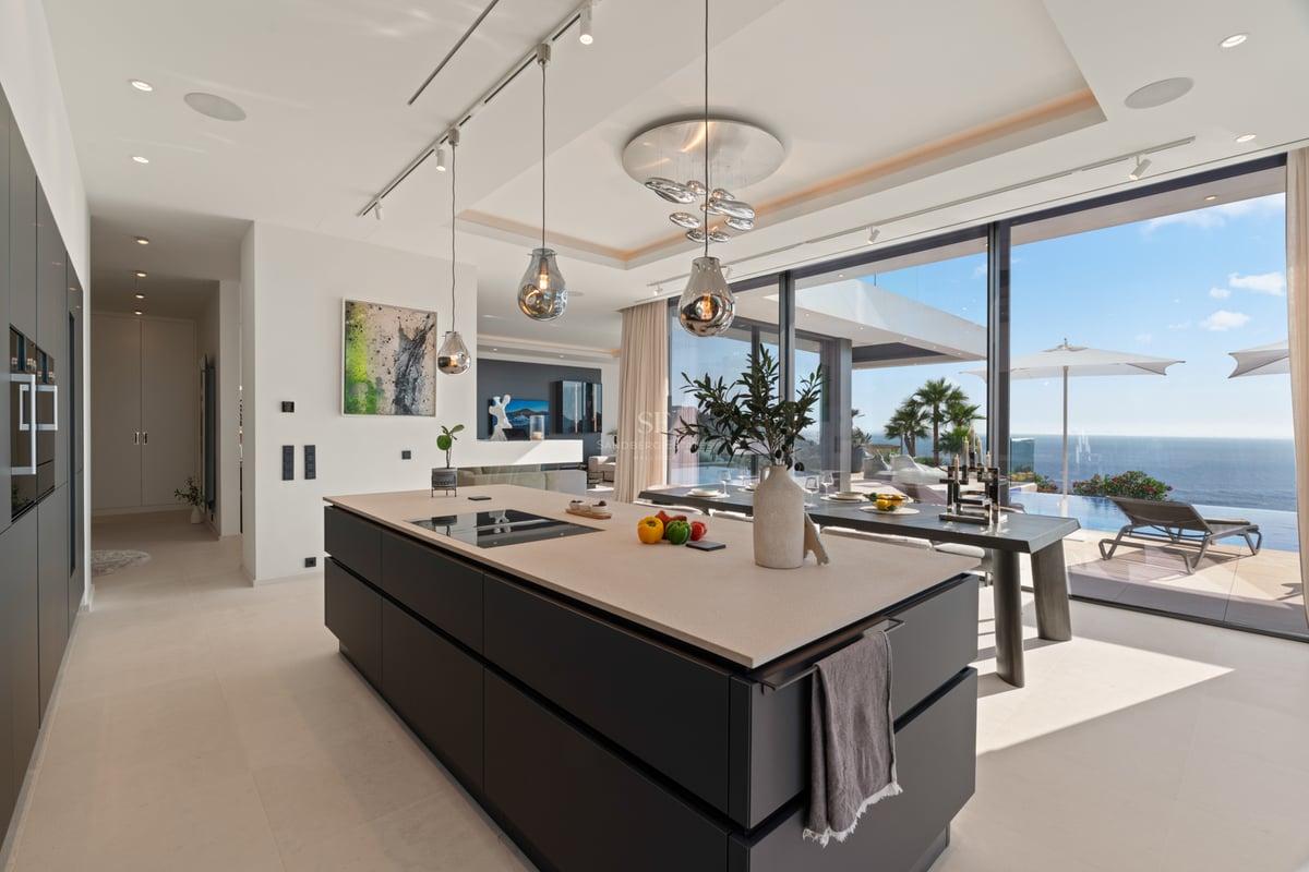 Cuisine moderne avec îlot central sombre, luminaires design en verre et baies vitrées donnant sur l'océan.