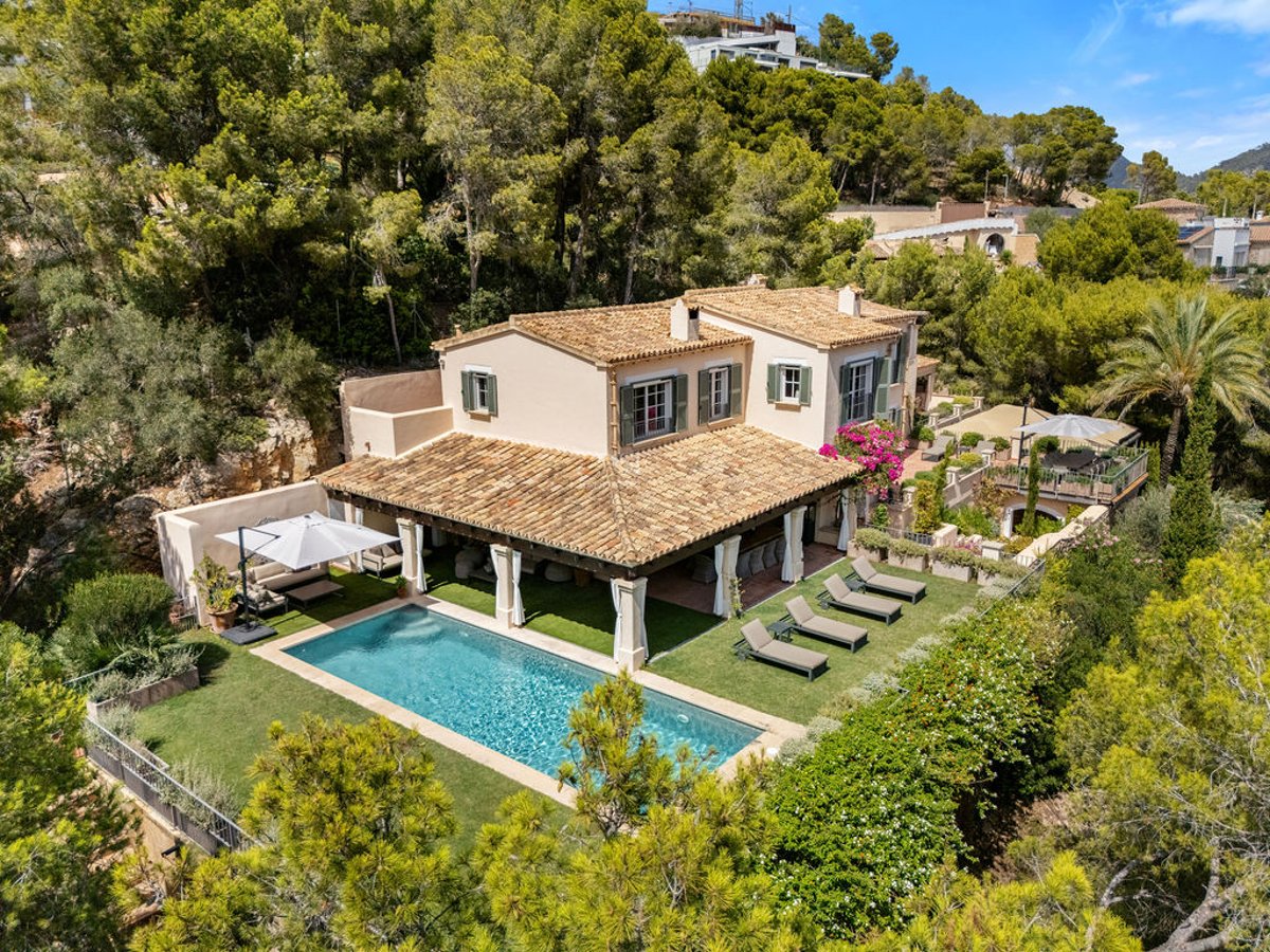 Vue aérienne d'une villa de luxe avec piscine turquoise, chaises longues et terrasse ombragée entourée de pins.