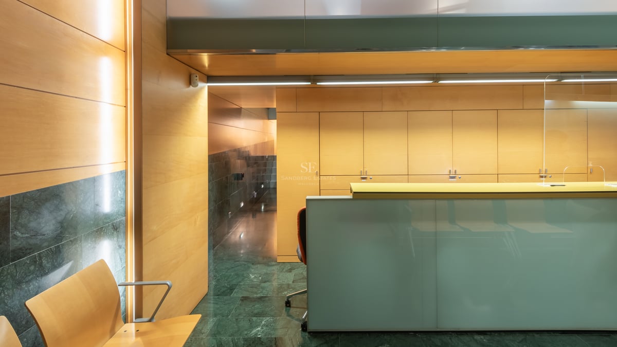 Modern reception desk with frosted glass, wood-paneled walls, and dark green marble flooring in a luxury building.