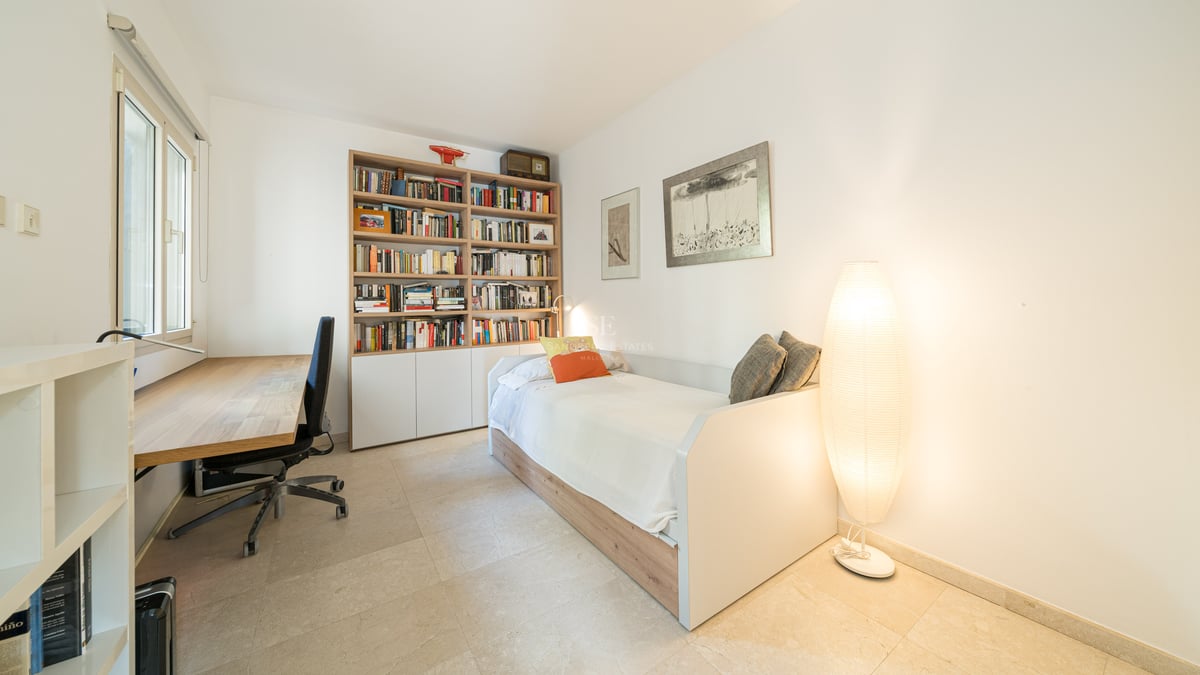 Chambre lumineuse comprenant un lit simple, une grande bibliothèque en bois, un bureau et un lampadaire design.