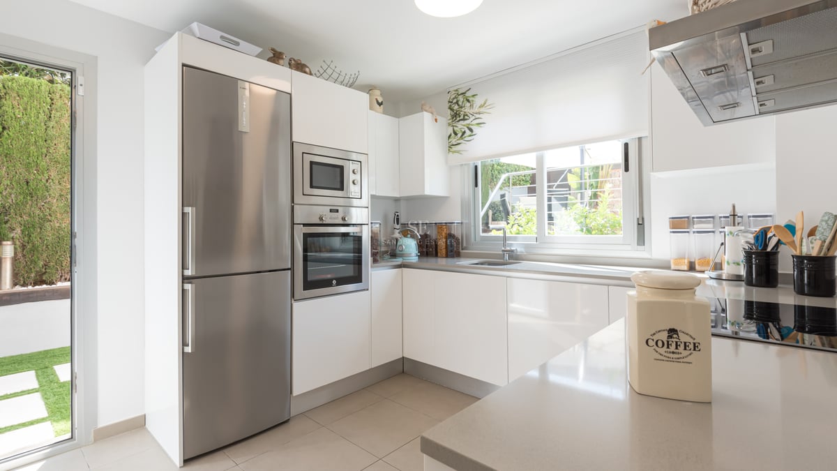 Cuisine moderne lumineuse avec armoires blanches, appareils en inox et porte vitrée donnant sur le jardin.