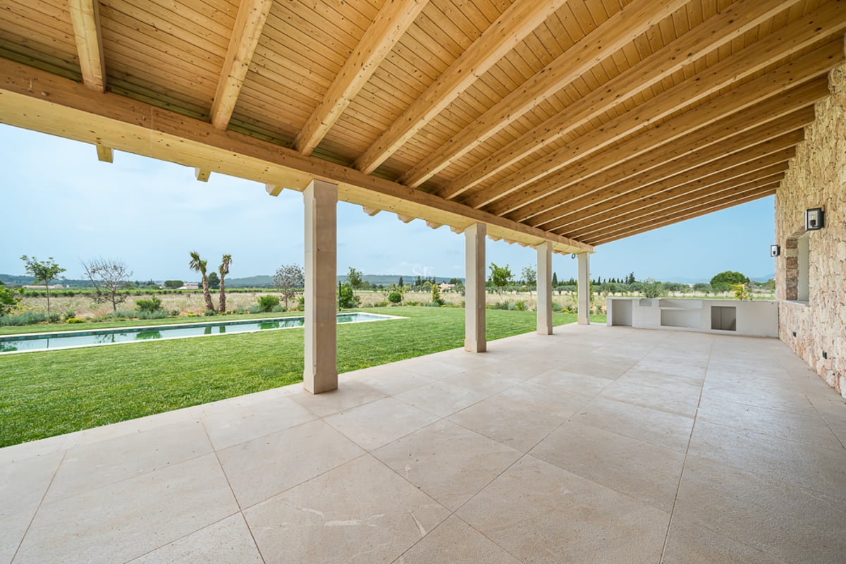 Large terrasse couverte avec dalles en pierre et plafond en bois donnant sur une pelouse et une piscine.
