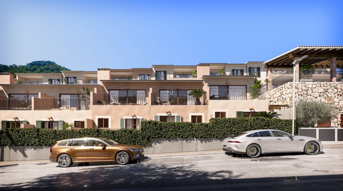 Modern apartment building with balconies, stone walls, and luxury cars parked on the street under a clear blue sky.