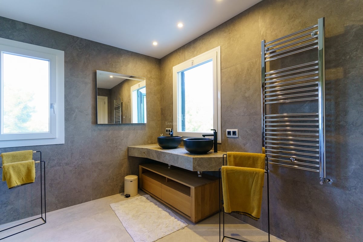 Salle de bain contemporaine avec murs en pierre grise, double vasque noire et grand sèche-serviettes.