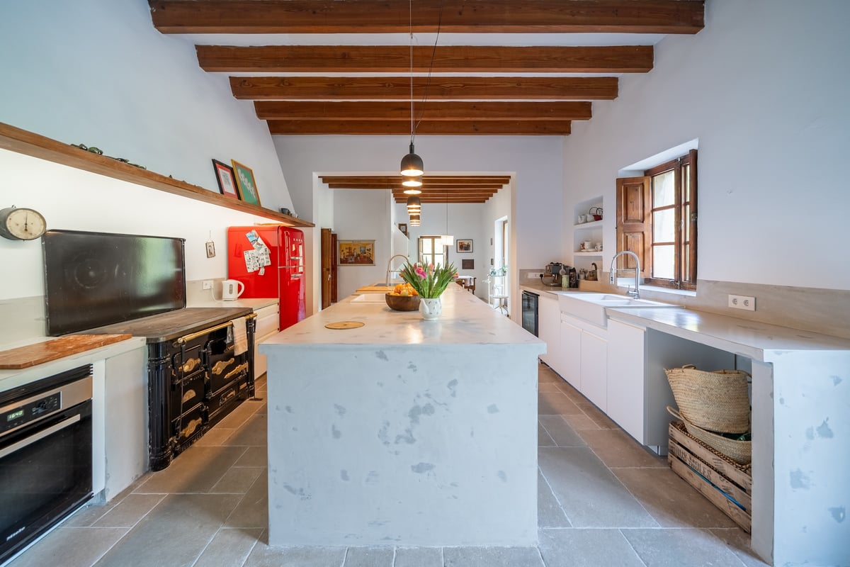 Grande cuisine avec îlot central blanc, poutres en bois apparentes, réfrigérateur rouge rétro et piano de cuisson.