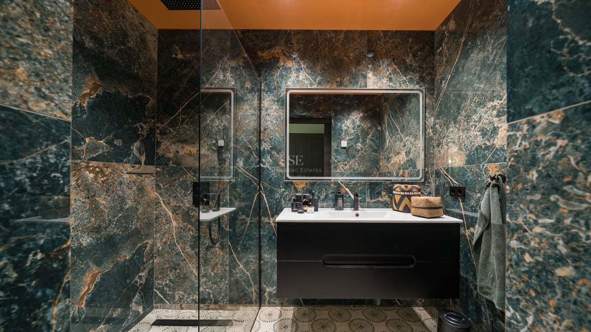 Salle de bain moderne avec carrelage effet marbre vert, meuble vasque noir et grand miroir éclairé.
