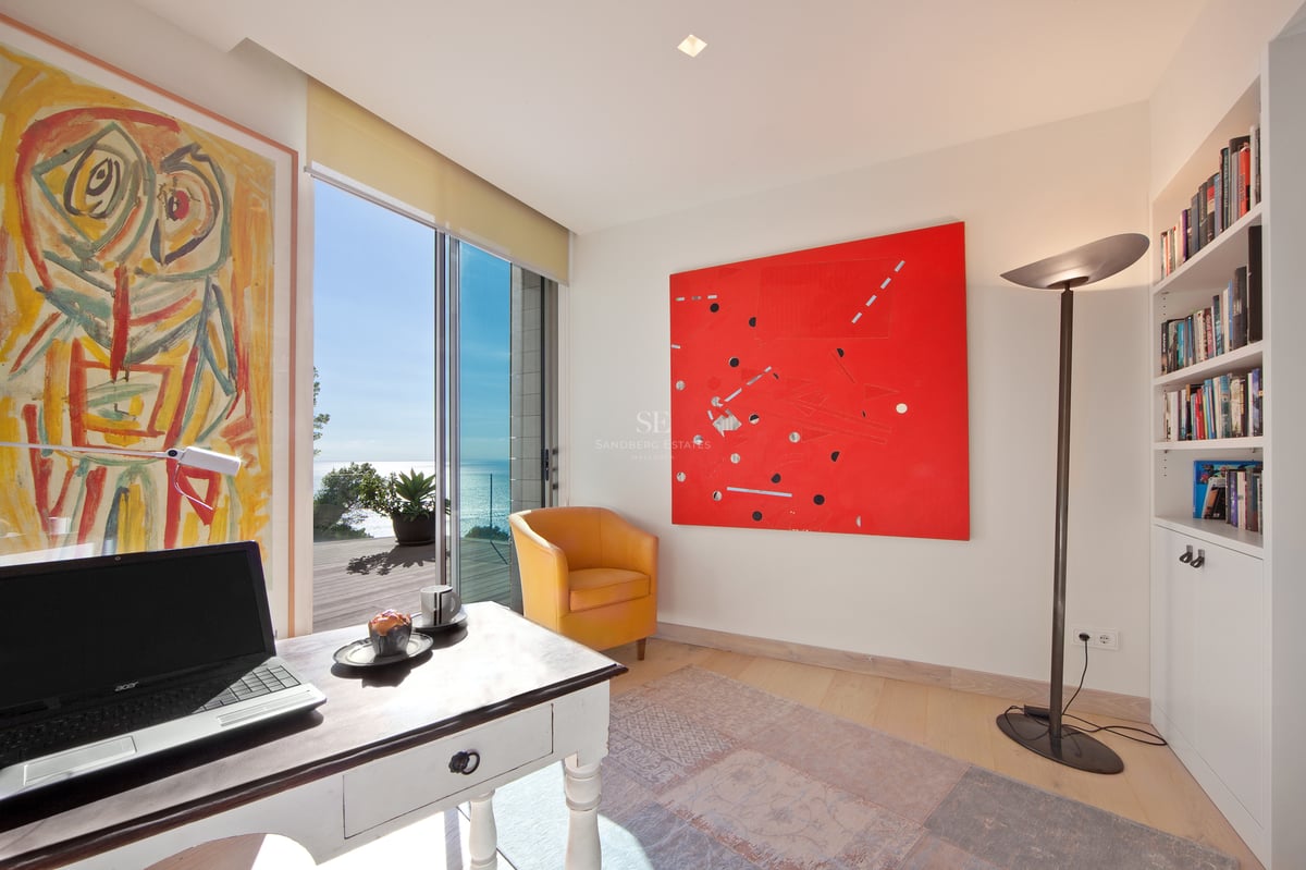 Bureau lumineux avec fauteuil jaune, art abstrait et baies vitrées donnant sur une terrasse face à la mer.