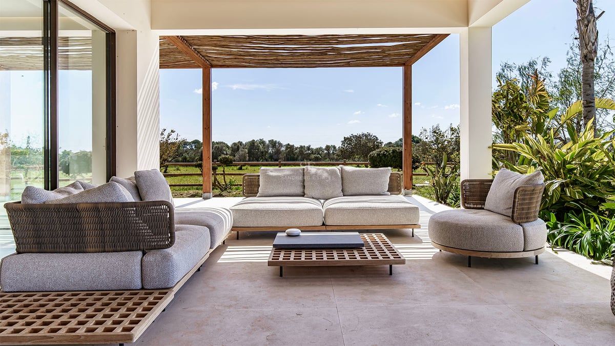 Salon de jardin moderne sur une terrasse en pierre abritée par une pergola en bois avec vue sur la campagne.