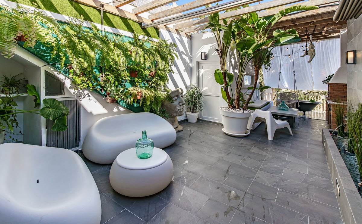 Terrasse extérieure avec canapés blancs arrondis, plantes luxuriantes, sol en pierre grise et pergola en bois.