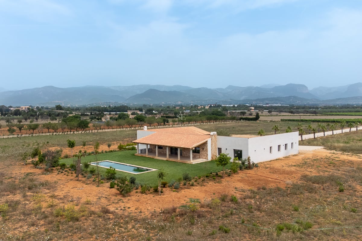 Vue aérienne d'une villa blanche avec piscine, toit en terre cuite et pelouse face aux montagnes.