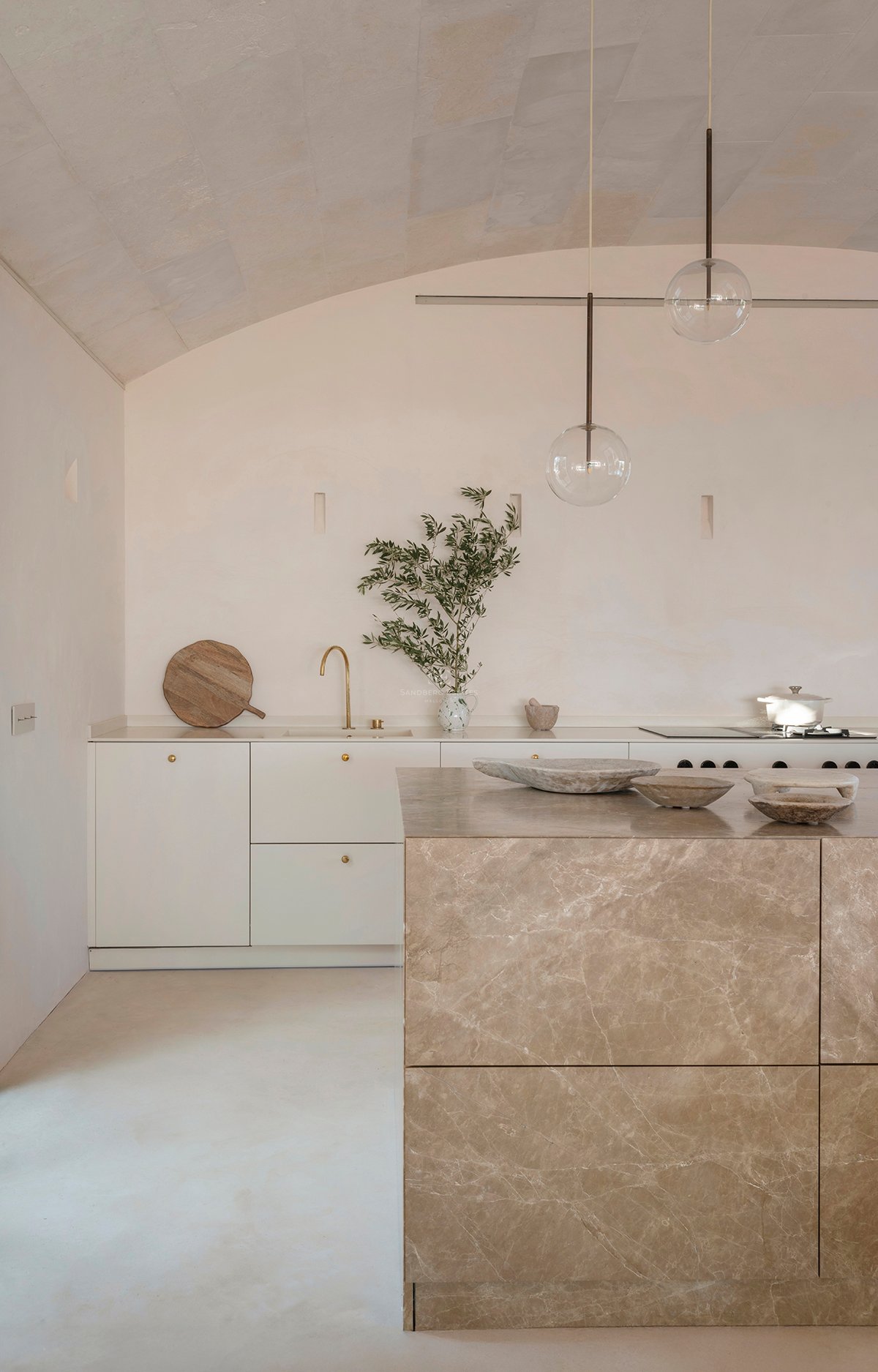 Minimalist kitchen with a large marble island, brass fixtures, and a textured vaulted ceiling in sand tones.