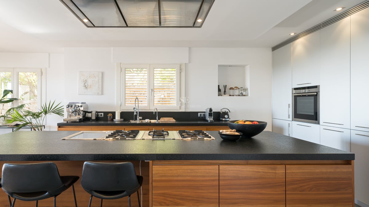 Cuisine contemporaine dotée d'un grand îlot en pierre noire, plaques de cuisson au gaz, menuiserie en noyer et meubles blancs.