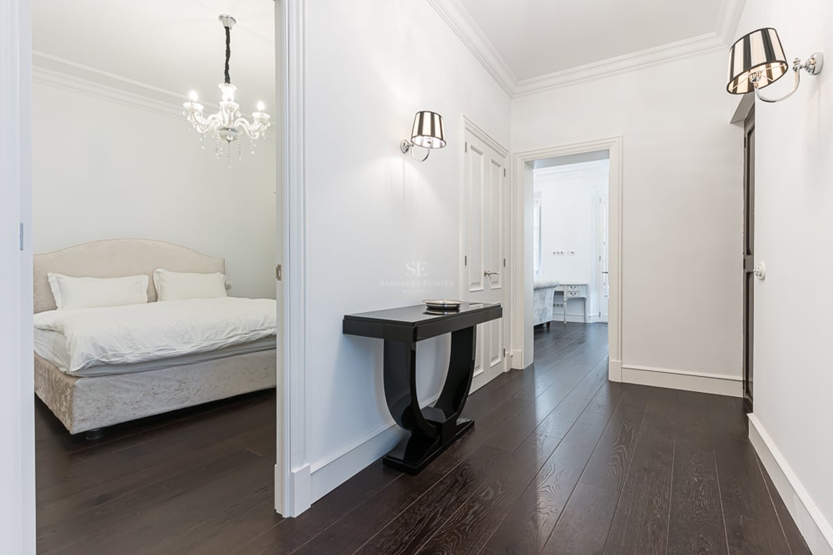 Couloir lumineux avec parquet foncé, console noire et vue sur une chambre avec lustre en cristal.