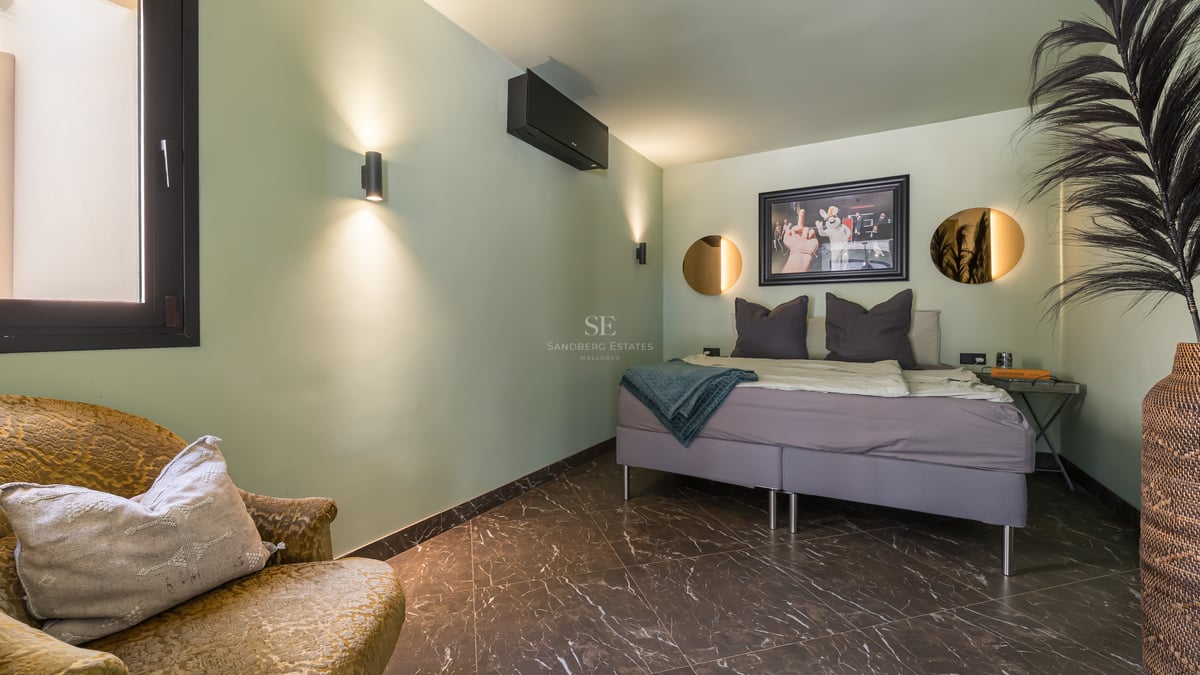 Chambre avec murs vert sauge, sol en marbre sombre, lit gris, fauteuil en velours et miroirs ronds.