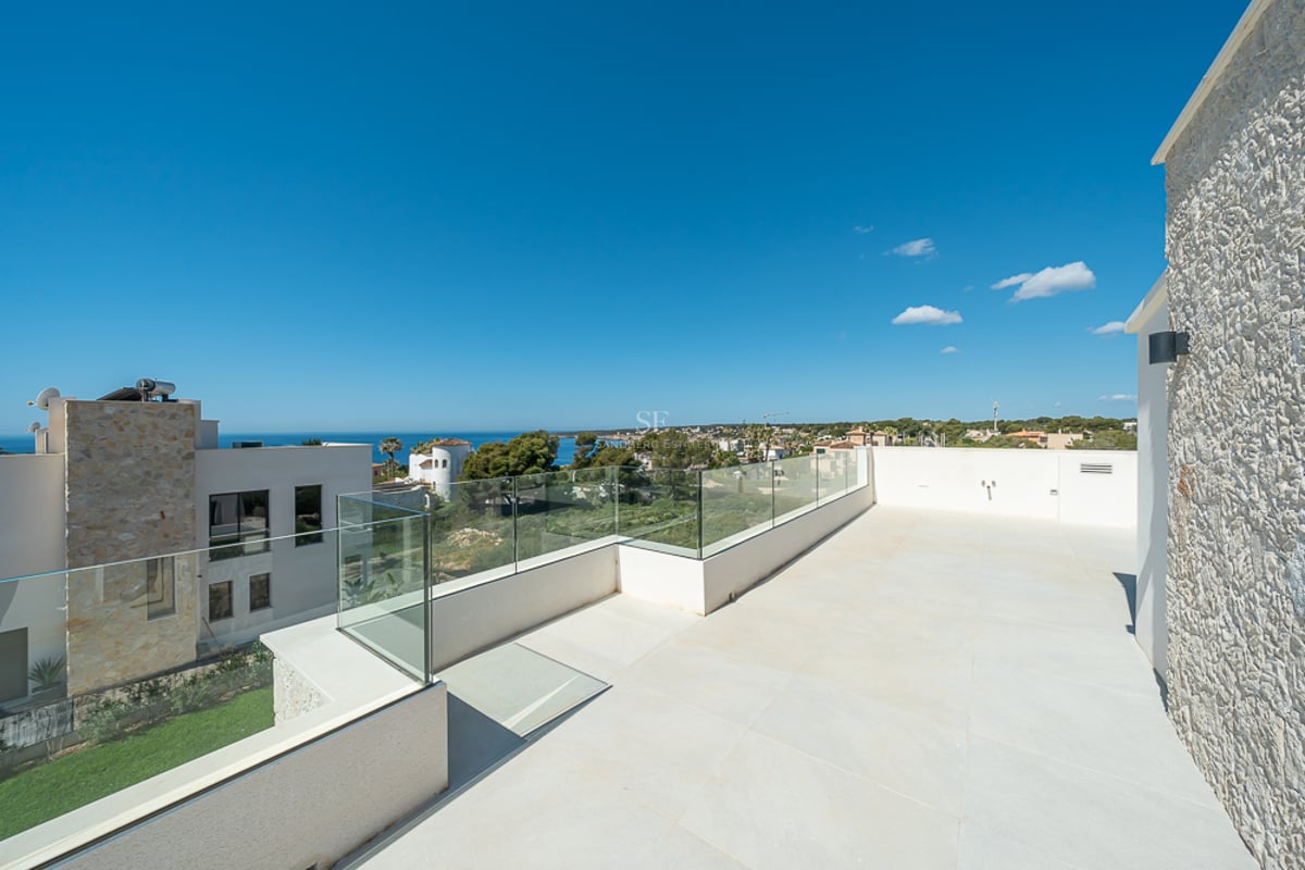 Grande terrasse moderne avec garde-corps en verre, sol en pierre claire et vue imprenable sur la mer Méditerranée.