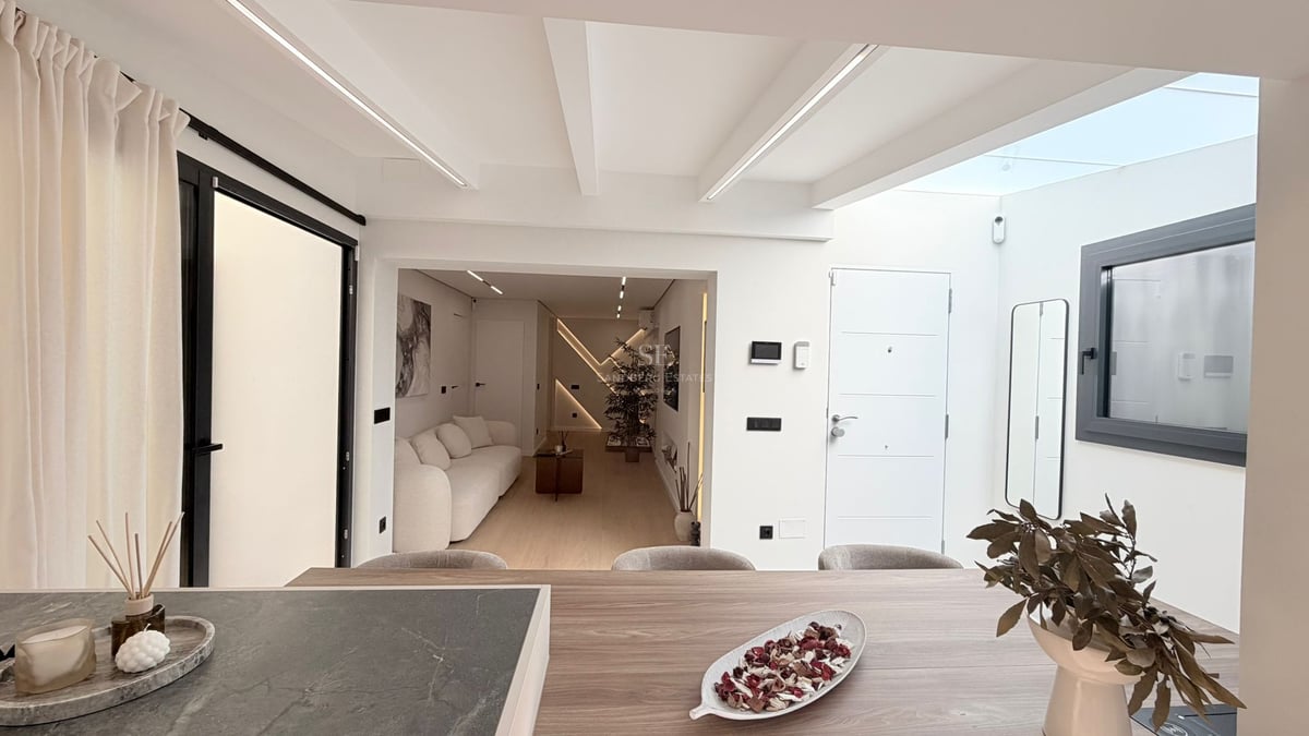 Intérieur moderne et lumineux avec canapé blanc, textures en bois et puits de lumière éclairant le salon et l'entrée.