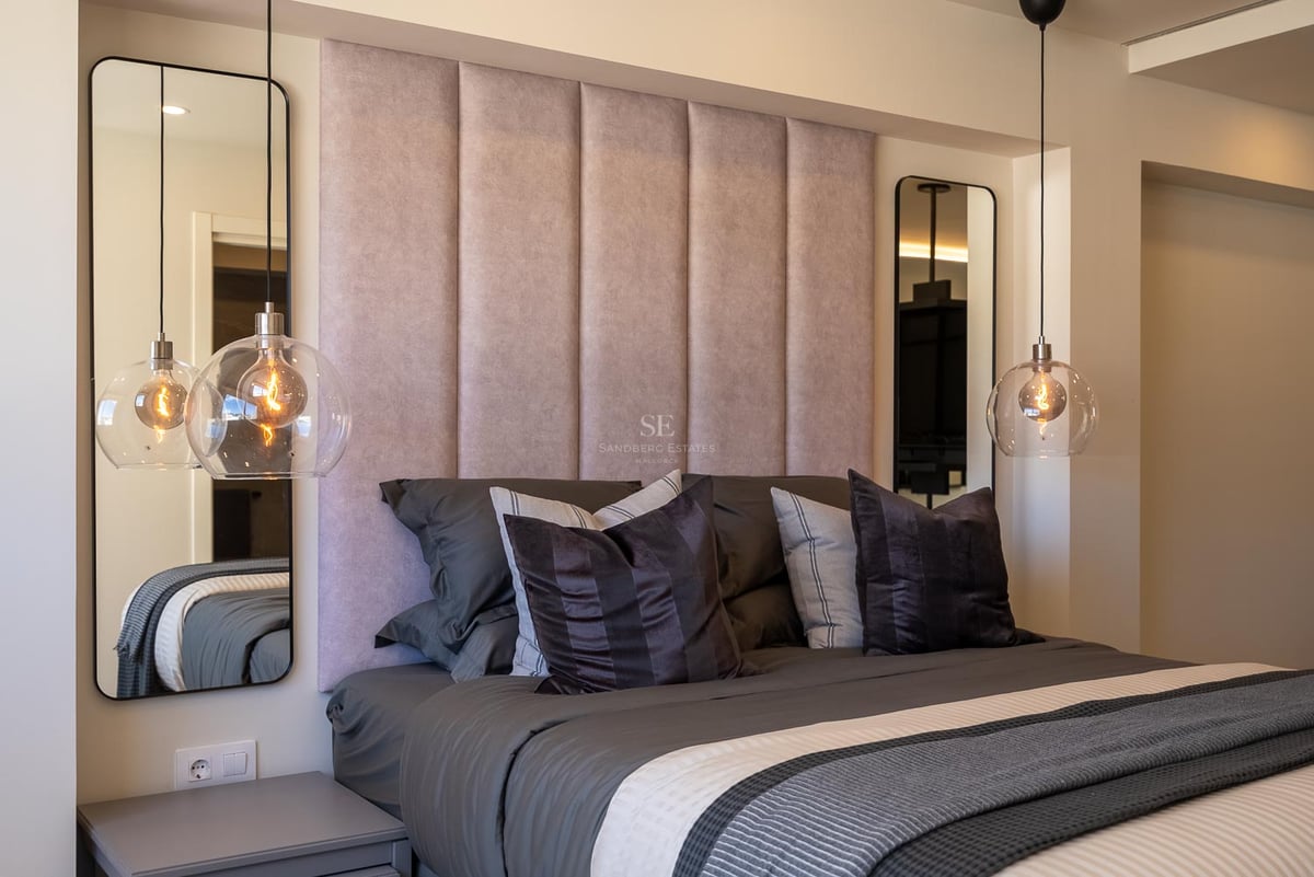 Lit avec tête de lit rose, suspensions en verre et miroirs symétriques dans une chambre de luxe moderne.
