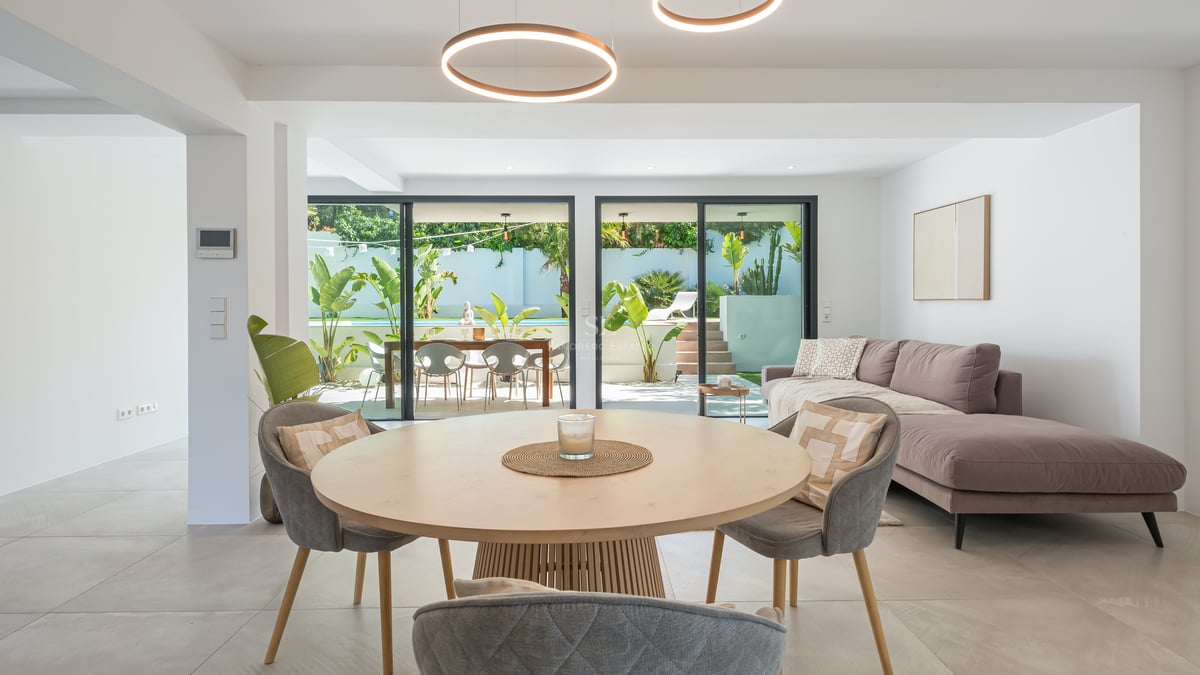 Salon et salle à manger contemporains avec luminaires LED circulaires, canapé gris et vue sur piscine et jardin.