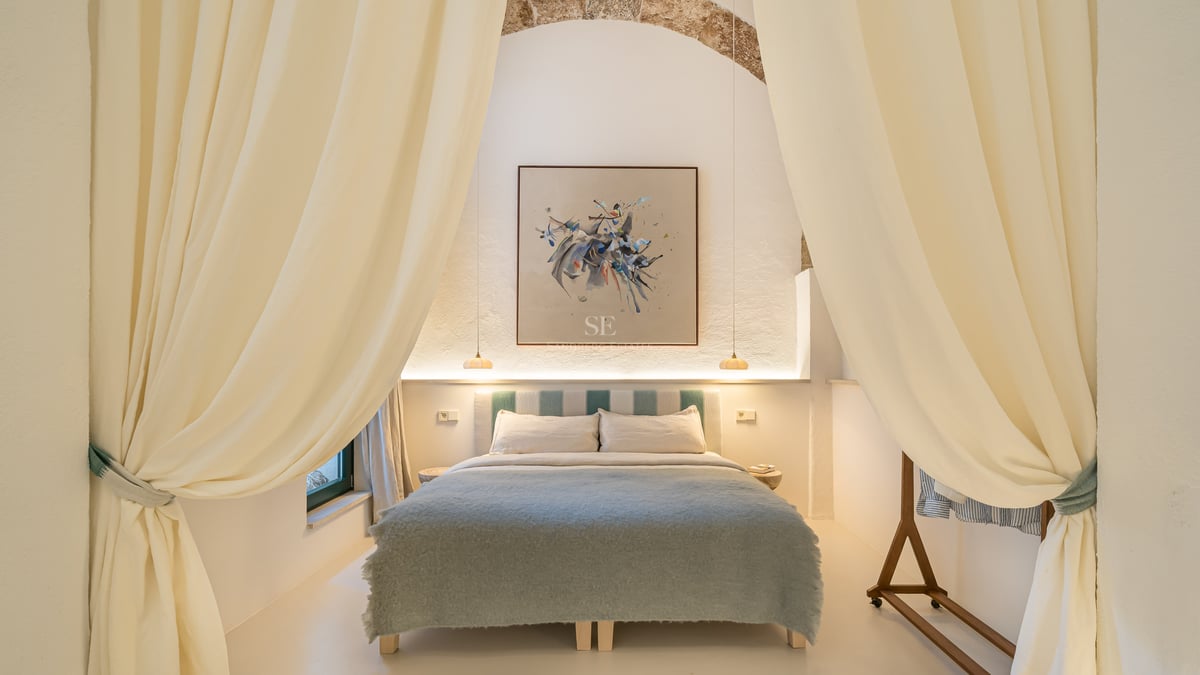 Chambre élégante avec arche en pierre, art abstrait et literie bleu doux encadrée par de grands rideaux crème.