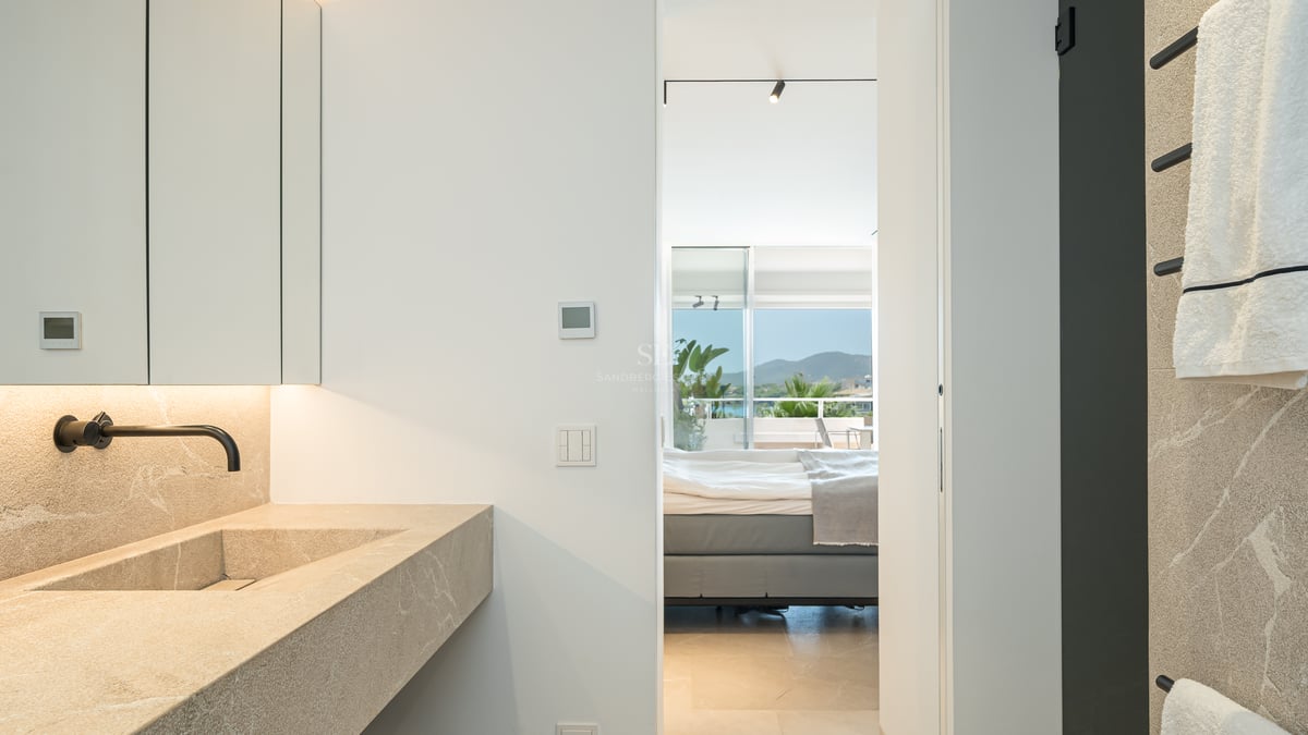 Salle de bain moderne avec vasque en pierre et robinet noir, vue sur la chambre et les montagnes au loin.
