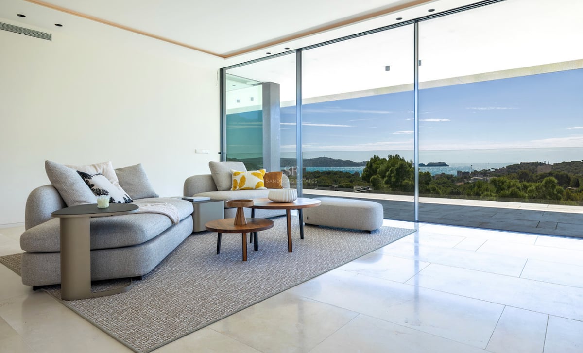 Salon lumineux avec canapé gris, tables en bois et baies vitrées offrant une vue imprenable sur la mer.