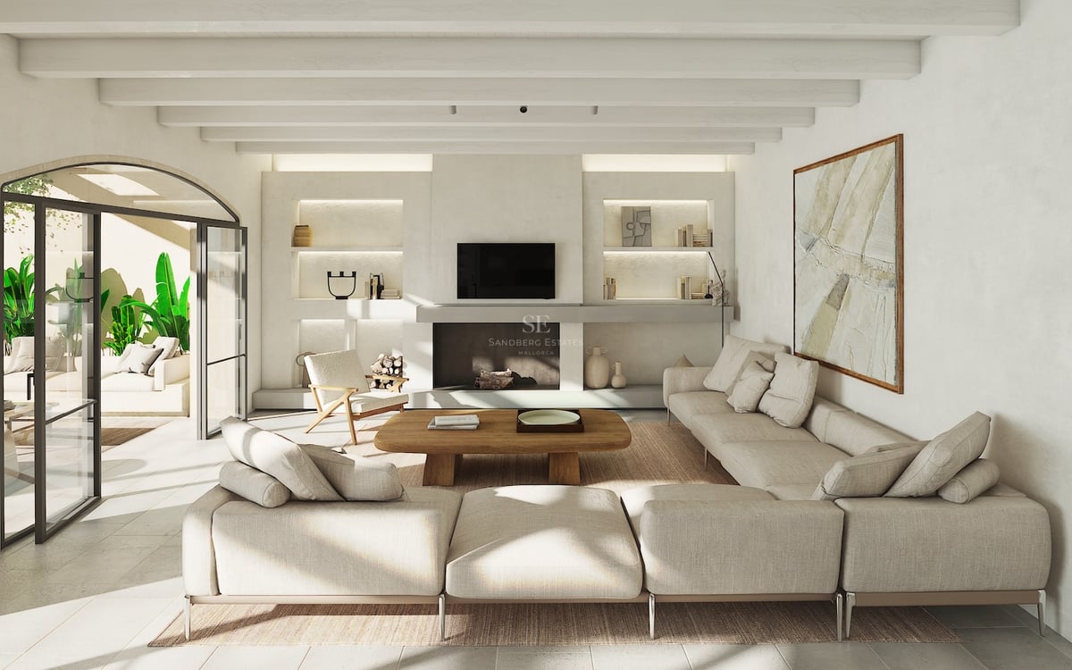 Salón luminoso con sofá modular beige, techos con vigas de madera y salida arqueada a una terraza con plantas.