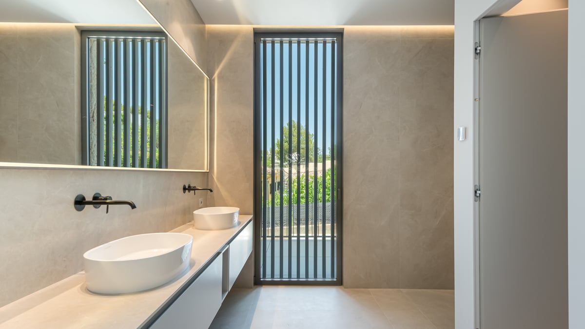 Salle de bain moderne avec double vasque ovale, robinetterie noir mat et grand miroir rétroéclairé.